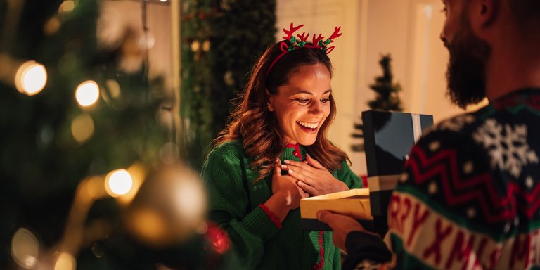 Frau in Weihnachtspulli erhält von einen Mann ein Geschenk und freut sich