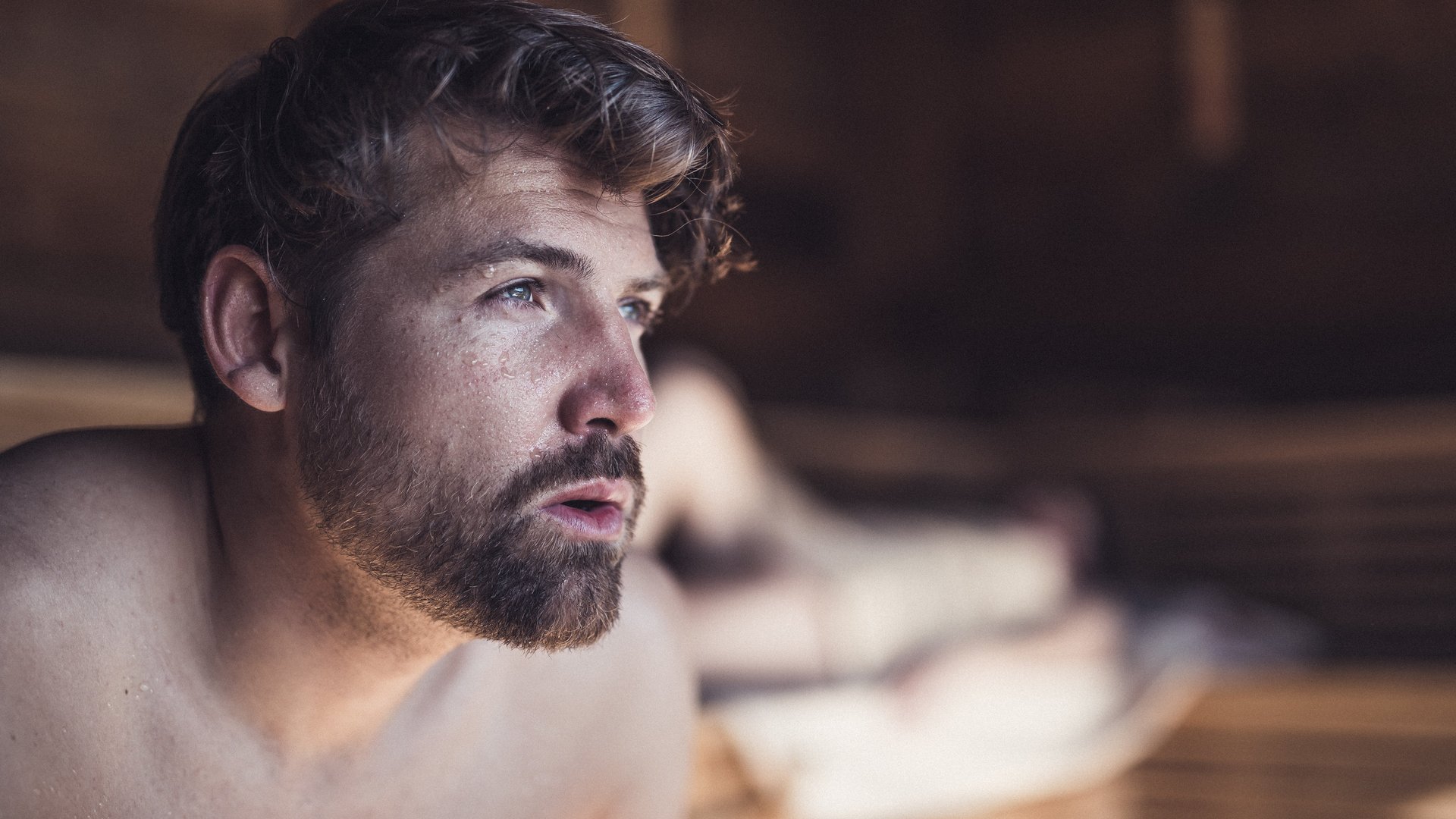 Junger Mann mit Bart schwitzt in der Sauna