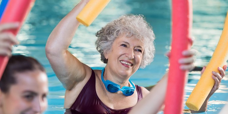 Frau im Seniorenalter mit Poolnudel im Schwimmbecken